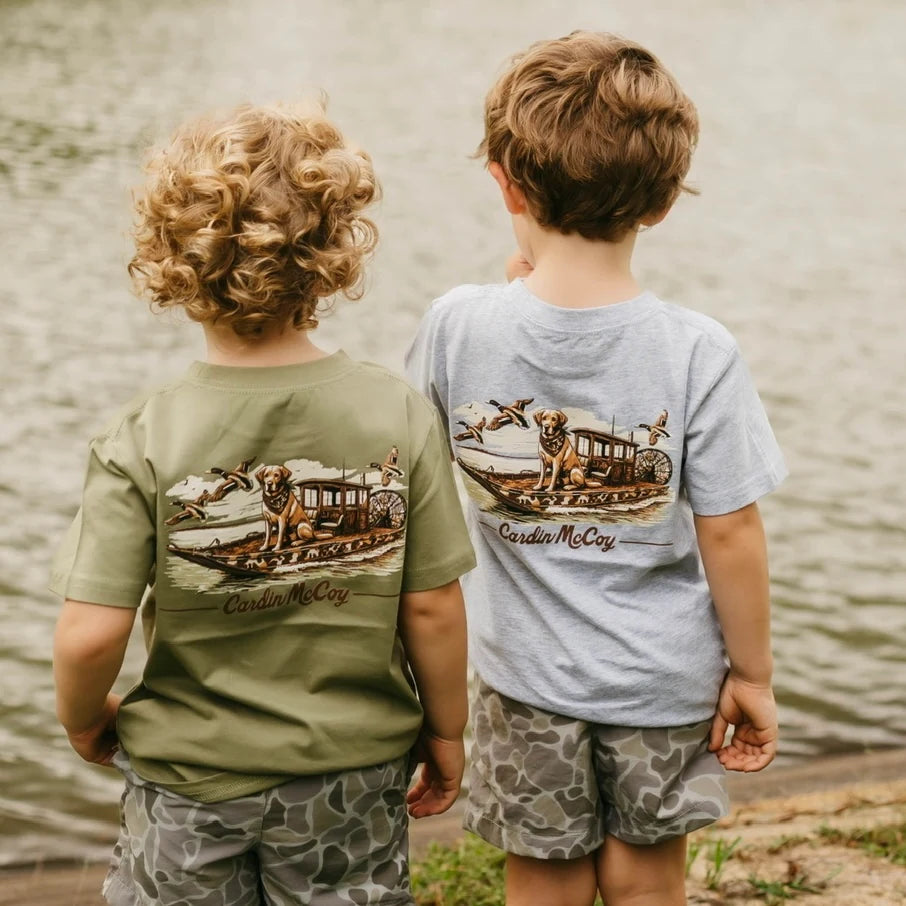 Two boys wearing Cardin McCoy Duck Boat graphic tees beside a pond.