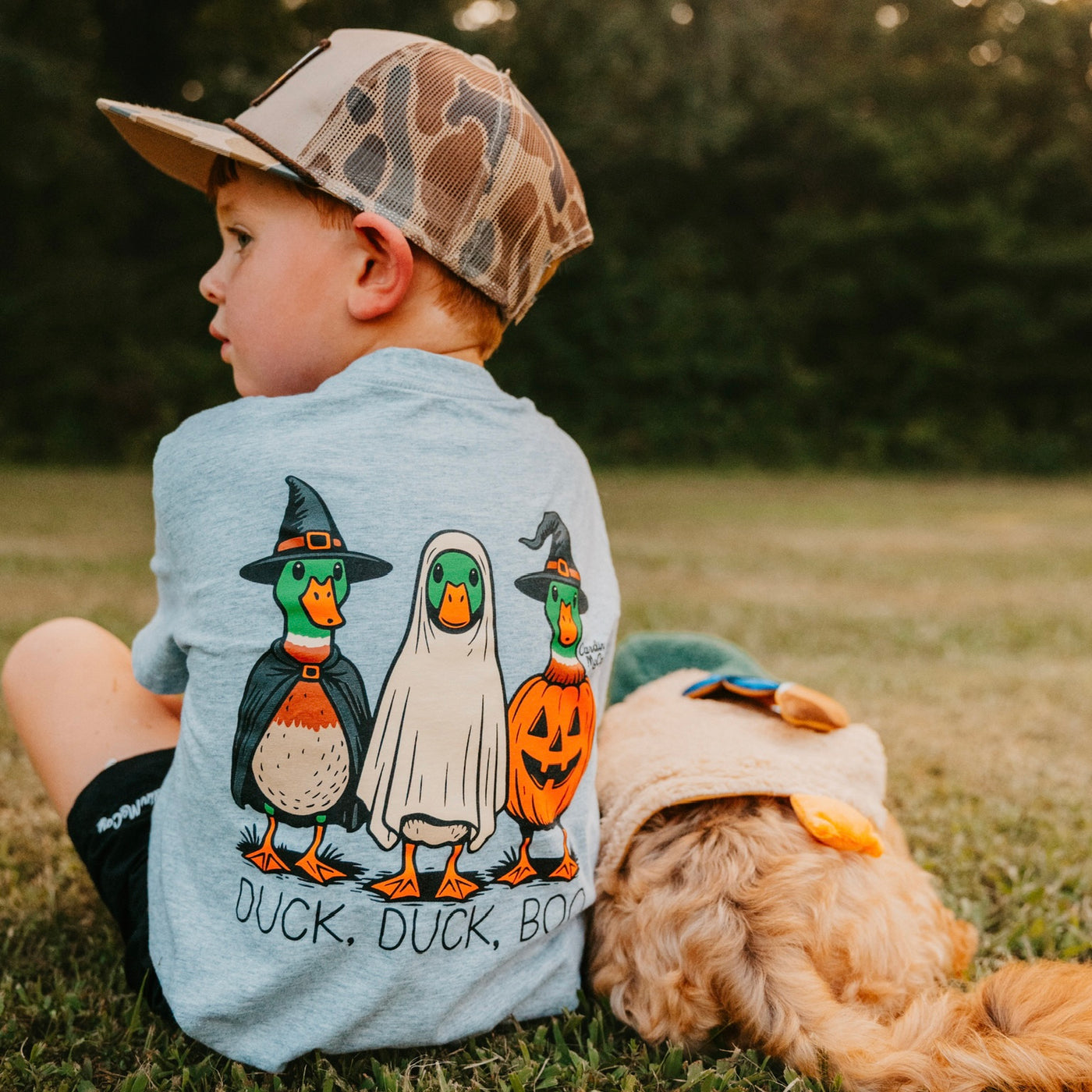 Child wearing the Cardin McCoy Duck, Duck, Boo tee beside a dog in a pumpkin costume.