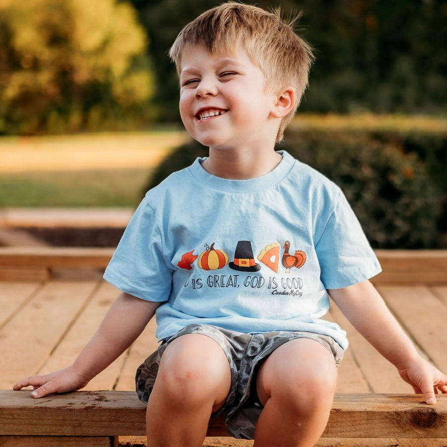 Smiling child wearing a blue Cardin McCoy Thanksgiving tee on a wooden bench.